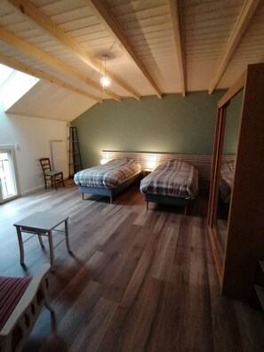 Une chambre avec deux lits, un plancher en bois, une fenêtre et une chaise.
