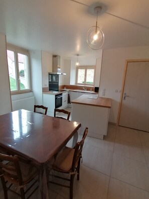 A modern kitchen with a dining table and chairs, a built-in oven, and a pendant light. - Gîte du Bois de Reine (Frébuans)