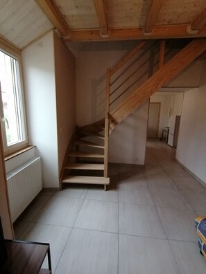 A room with a wooden staircase, a radiator, and a window. - Gîte du Bois de Reine (Frébuans)