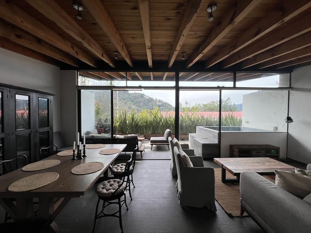 Un interior moderno con comedor, asientos y ventanas amplias con vistas a zonas verdes y colinas.