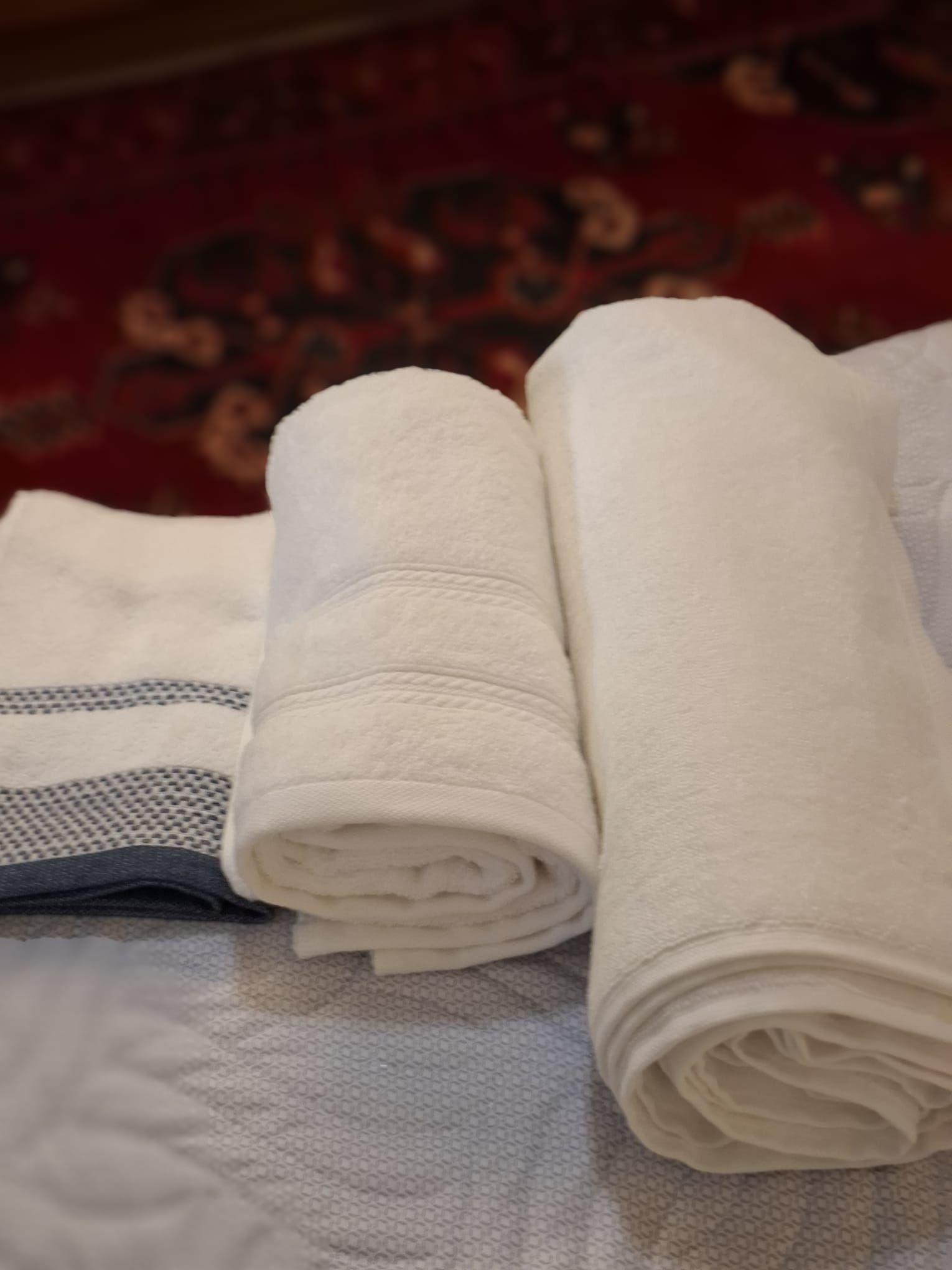 A stack of folded towels on a bed with a patterned carpet in the background.