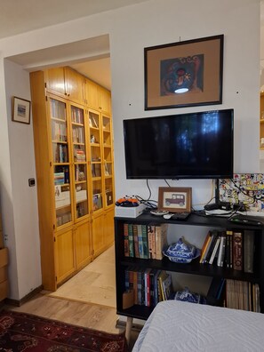 A room with a television, bookshelf, and a wooden cabinet with glass doors.