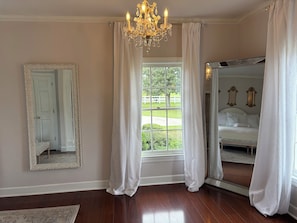 A room with a large mirror, a chandelier, and a view of a green landscape through a window. - The Ultimate Masters Stay - Manor + Event Venue in Augusta - near Airport & 520 (Augusta)