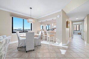 A modern living room with a dining area, large windows, and a view of the cityscape. - "Broadmoor #705" --- New! Beachfront 3BR, Stunning Gulf Views, Pool, Hot Tub (Orange Beach)