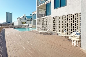 A wooden deck with sun loungers and a pool, overlooking a cityscape. - "Broadmoor #705" --- New! Beachfront 3BR, Stunning Gulf Views, Pool, Hot Tub (Orange Beach)