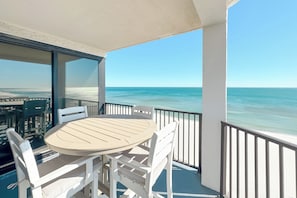Ein Balkon mit Tisch und Stühlen mit Blick auf Strand und Meer.