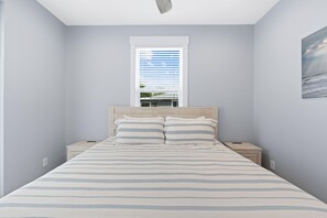 A bedroom with a bed, two bedside tables, a window with blinds, and a painting on the wall. - The Turtle Nest (Fort Myers Beach)