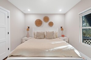 A bedroom with a bed, two bedside tables, a window, and wall decor. - Oasis on Ohio Ave (Fort Myers Beach)