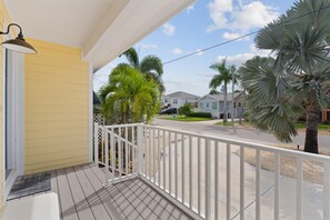 A wooden porch with a white railing, overlooking a street with houses and palm trees. - Oasis on Ohio Ave (Fort Myers Beach)
