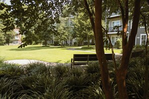 A well-maintained lawn with a bench, surrounded by trees and buildings in the background. - One Tree Hill Bridge | 3BR 3.5BA + Garage | Walk to Riverwalk, Live Oak Pavilion (Wilmington)