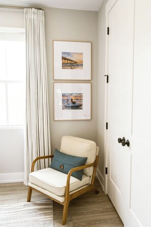 A room with a chair, a door, and two framed pictures on the wall. - One Tree Hill Bridge | 3BR 3.5BA + Garage | Walk to Riverwalk, Live Oak Pavilion (Wilmington)