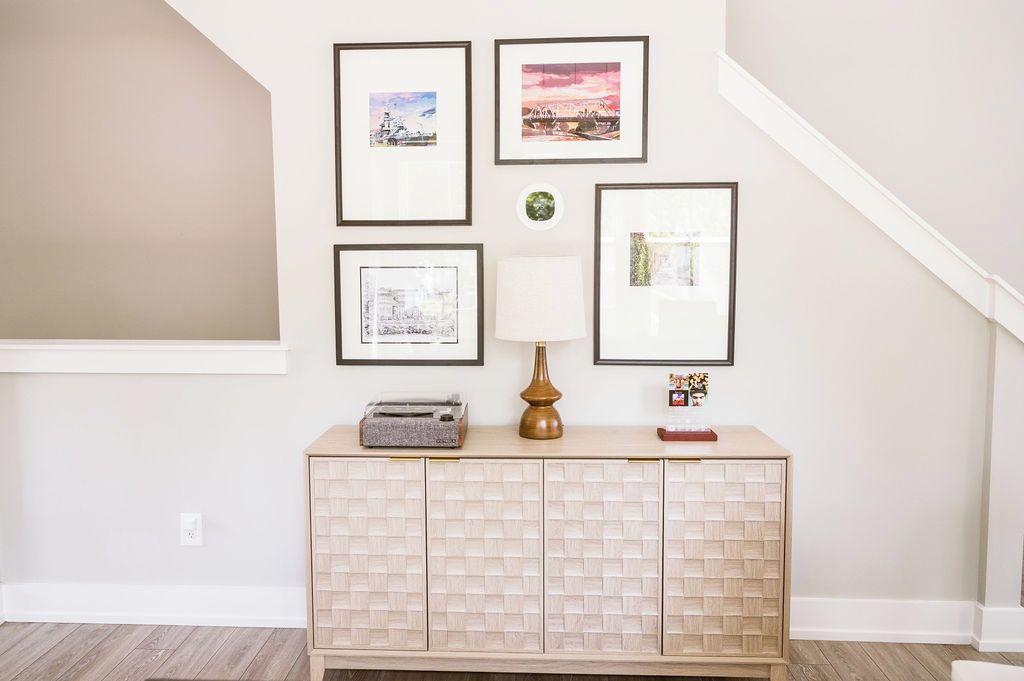 A room with a light-colored cabinet, a lamp, and framed pictures on the wall.