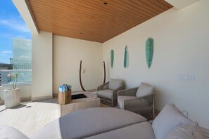 A modern lounge with a wooden ceiling, a large window, and a seating area with two chairs and a sofa. - Beachfront 2BR Penthouse, Private Rooftop Jacuzzi (San José del Cabo)