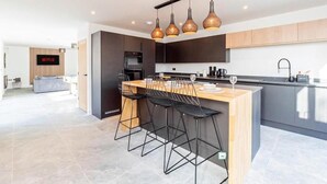 Cozinha moderna com ilha central, banquetas, iluminação pendente e sinalização da Netflix visível.