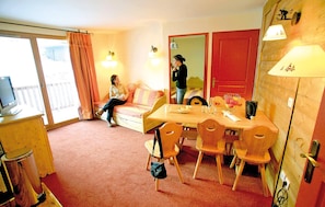 Ein Hotelzimmer mit Balkon, einer Couch, einem Esstisch mit Stühlen und einer roten Tür.
