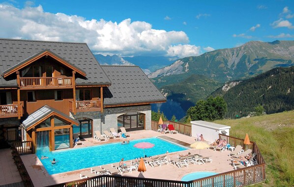A hotel with a pool, outdoor seating, and mountain views.