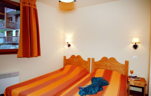 A hotel room with a bed, two wall-mounted lamps, a window with curtains, and a view of a building outside.
