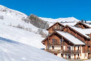 A wooden chalet with multiple balconies, situated on a snow-covered slope with a clear sky. - Proche du télésiège & commerces | Piscine | Sauna (Le Corbier)