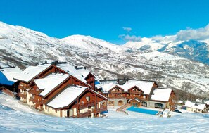 Ein schneebedecktes Bergresort mit Holzchalets und einem Schwimmbad.