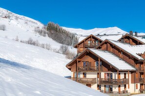A wooden chalet with multiple balconies, situated on a snow-covered slope with a clear sky.