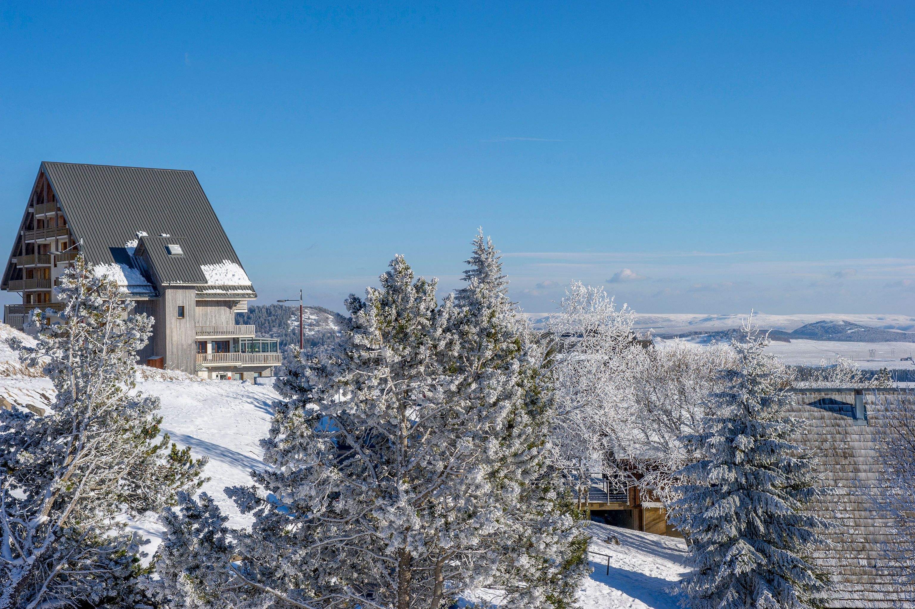 Een bergchalet bedekt met sneeuw, met een opvallende houten constructie en uitzicht op het besneeuwde landschap.