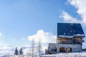 A multi-story building with a steeply pitched roof, a stone base, and a wooden upper section. - À 200m Espace Nordique | Vue Lac des Hermines (Besse-et-Saint-Anastaise)