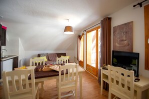 A cozy room with a dining table, chairs, a television, and a sofa. - À 200m Espace Nordique | Vue Lac des Hermines (Besse-et-Saint-Anastaise)