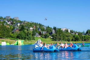 A group of people on blue watercrafts on a lake with houses in the background.
