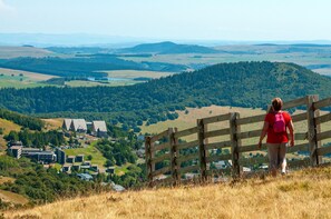 A person standing at a wooden fence overlooking a town with buildings and a hilly landscape.