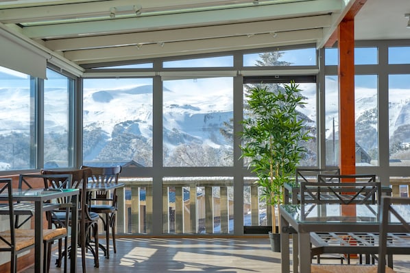 A room with large windows offering a snowy mountain view, wooden furniture, and a potted plant.