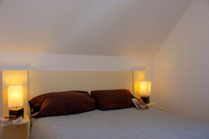 A hotel room with a bed, two bedside lamps, and a nightstand with a book and a phone.