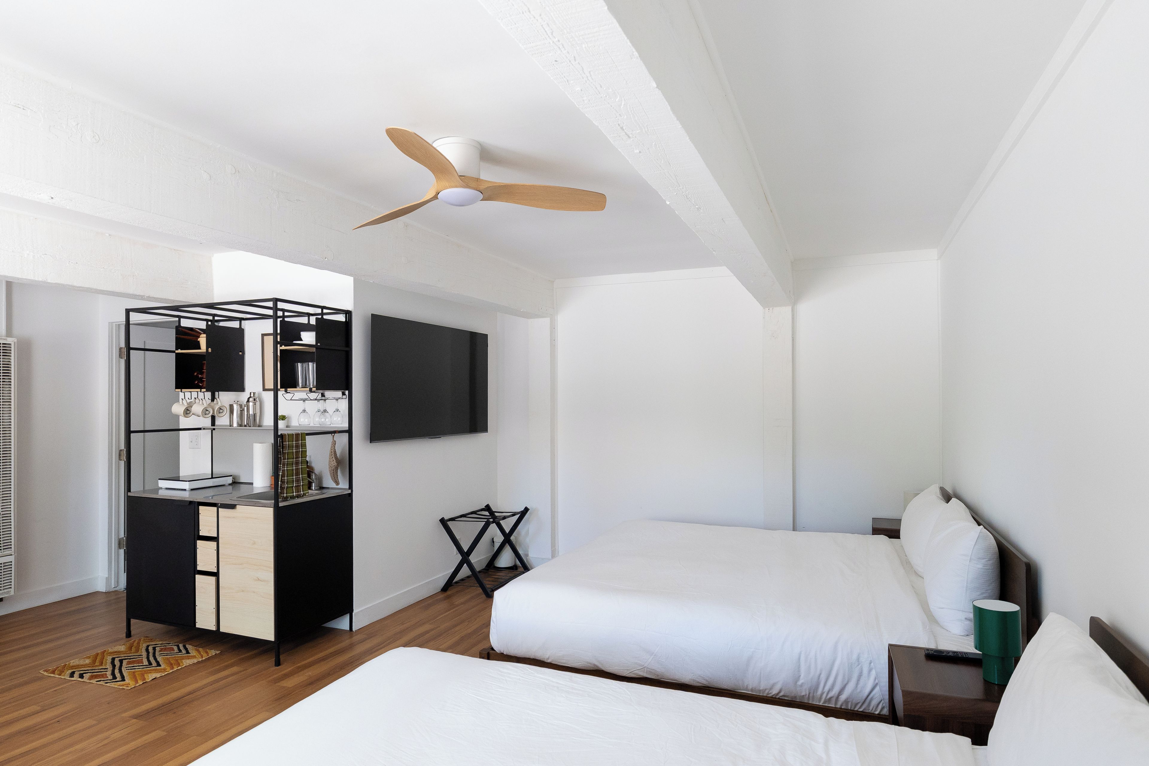 Una habitació d'hotel moderna amb un llit, un escriptori amb una cadira, un televisor fixat a la paret i un ventilador de sostre.
