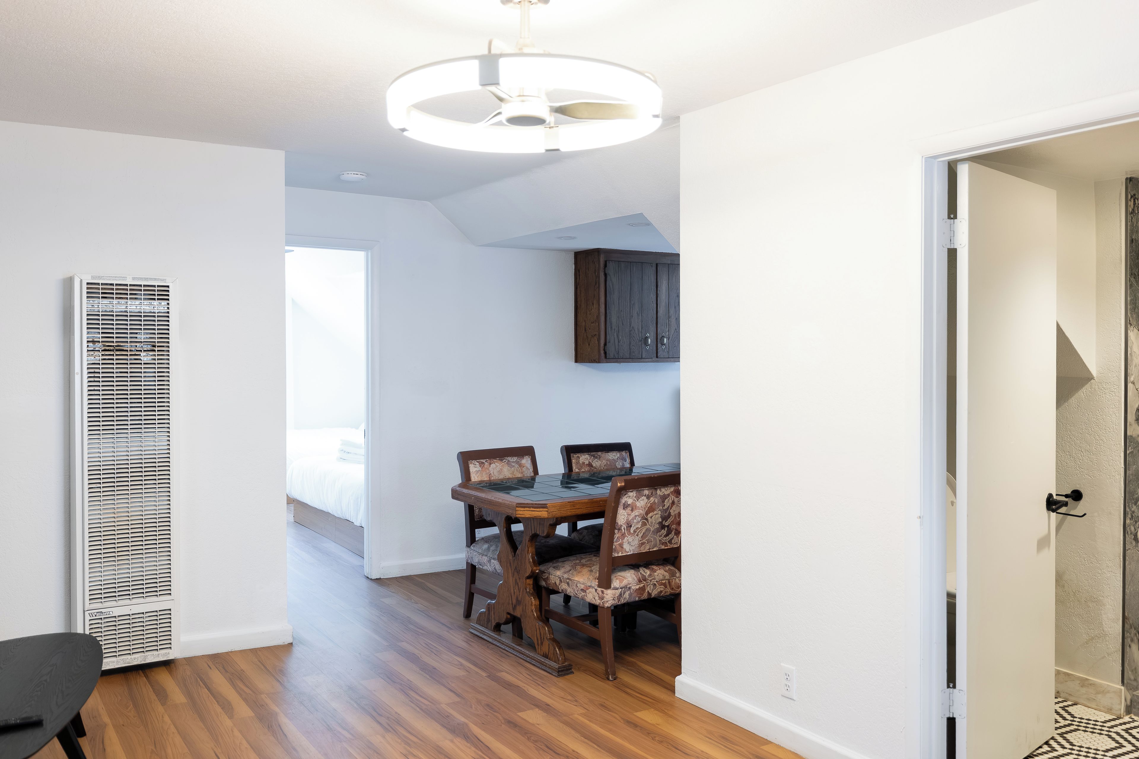 A room with a dining table and chairs, a ceiling light fixture, and a vent.