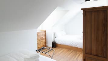 A bedroom with a sloped ceiling, a wooden wardrobe, a bed with white bedding, and a metal drying rack.