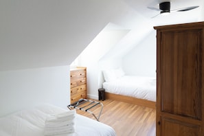 Quarto com teto inclinado, guarda-roupa de madeira, cama com roupa de cama branca e um varal de metal.