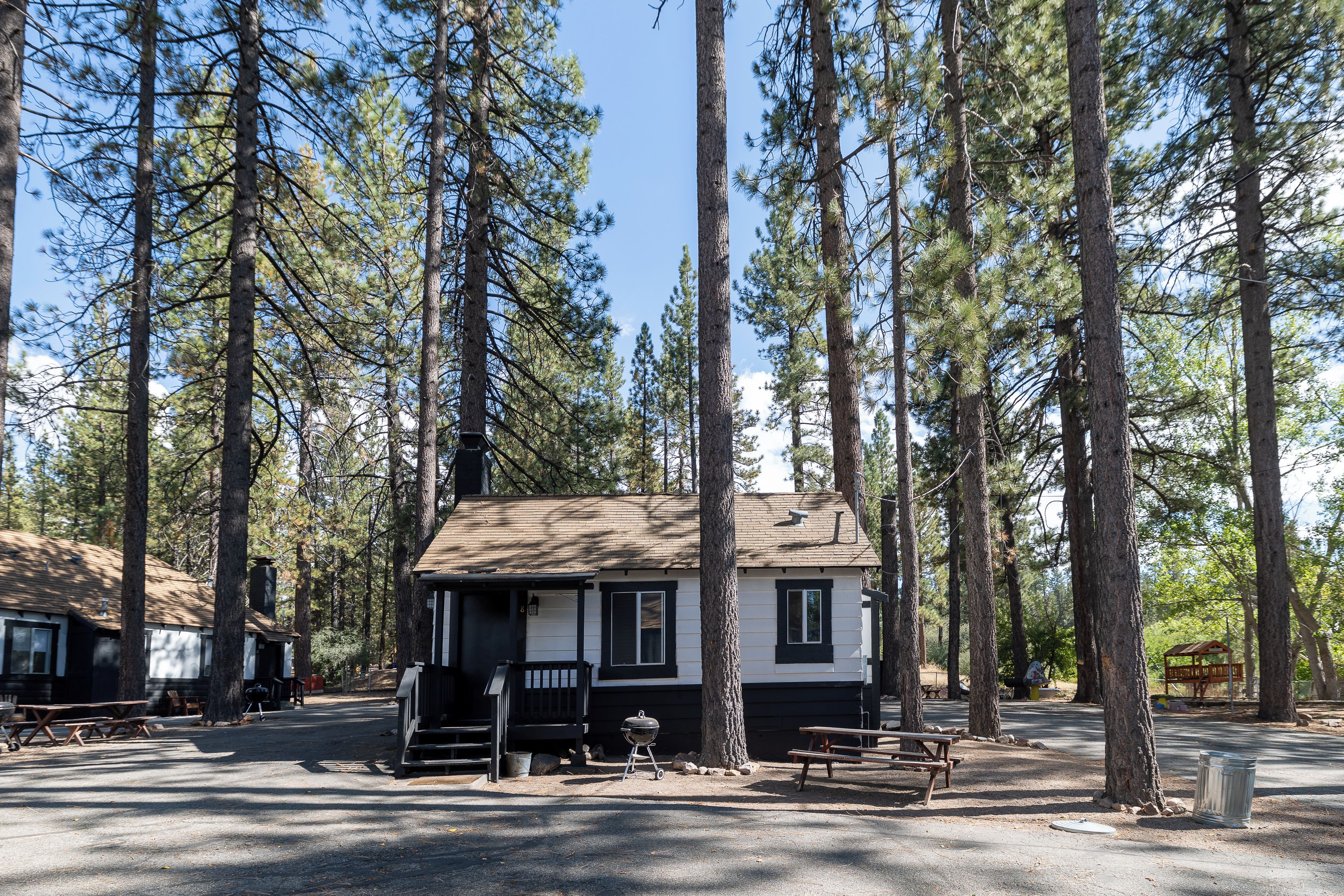 A cabin with a porch, a barbecue grill, and picnic tables in a forested campground.