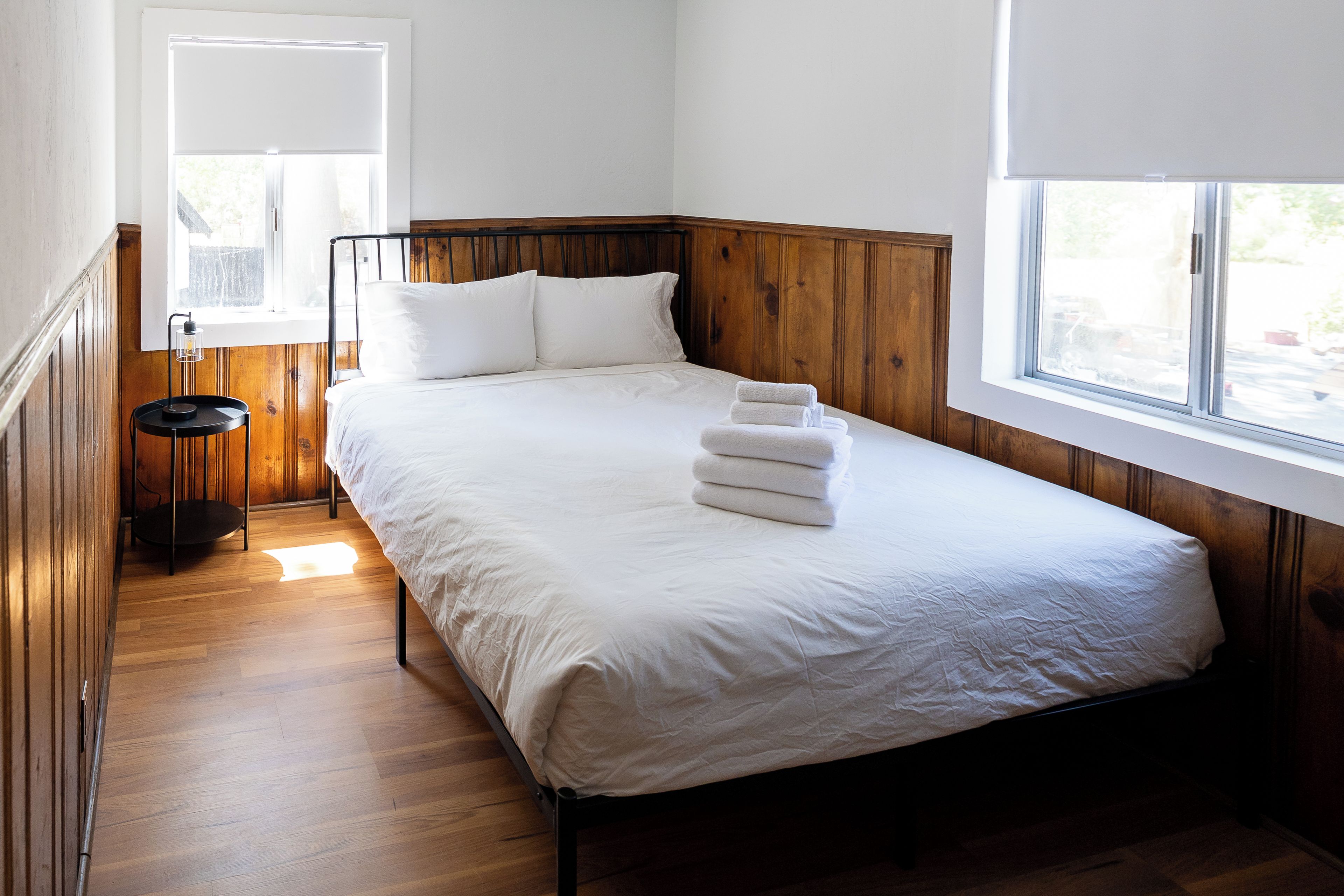 Una camera con un letto singolo, un poggiatesta in legno, un comodino con una lampada e una finestra con vista sull'esterno.