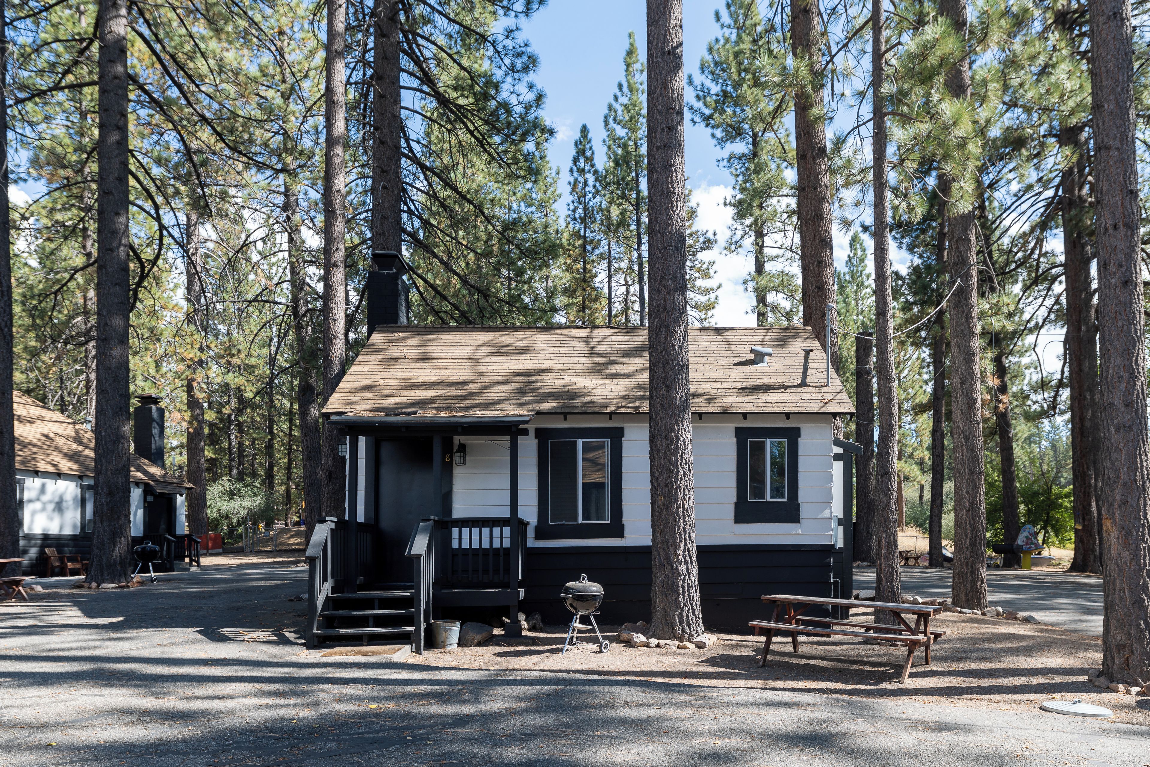 A cabin with a porch, a barbecue grill, and picnic tables in a forested campground.
