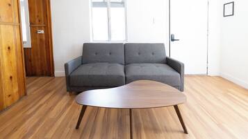 Ein Zimmer mit einem grauen Sofa, einem Holztisch und einem Holzschrank.