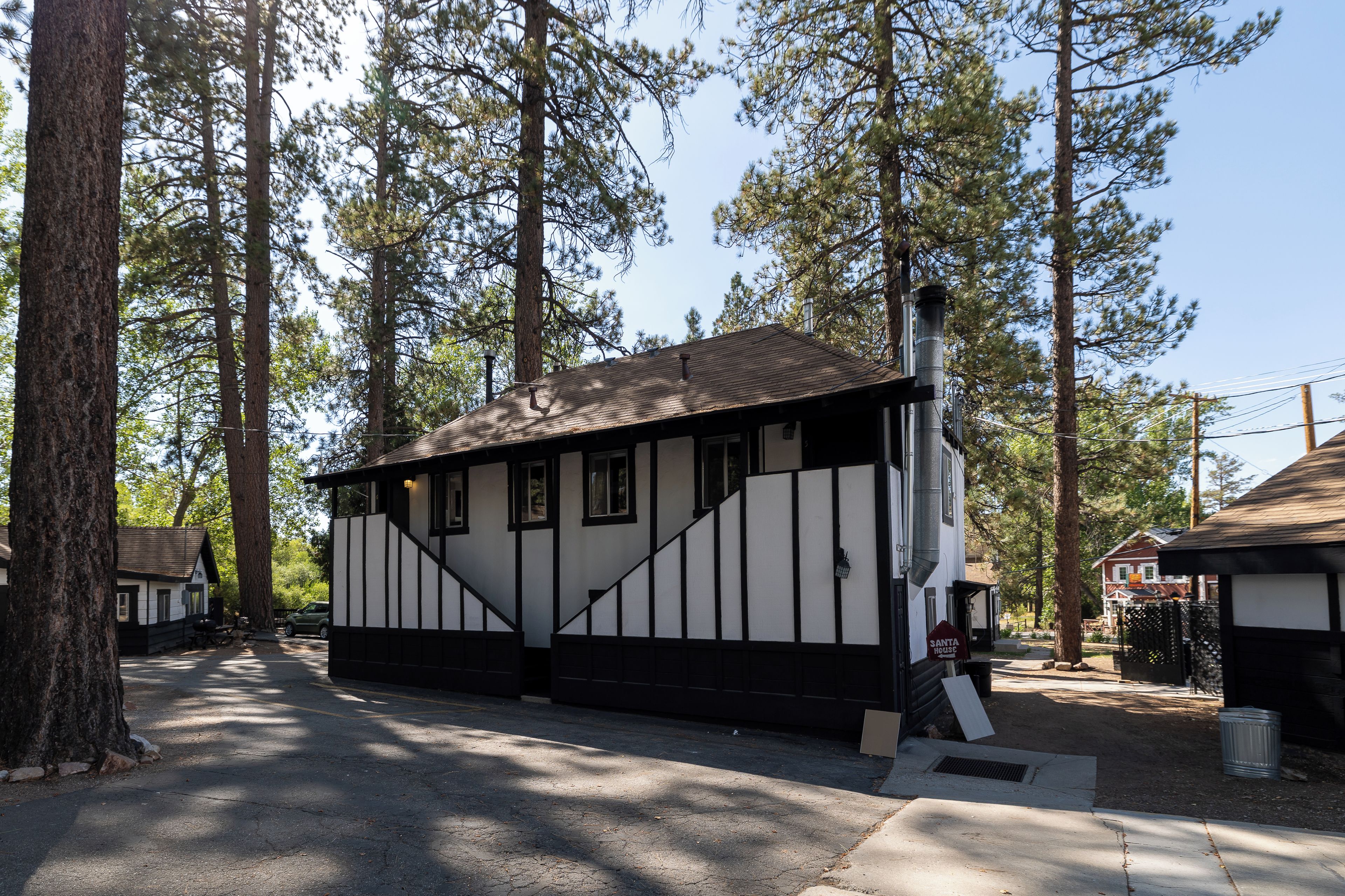 A small, single-story building with a black and white exterior, surrounded by tall pine trees.