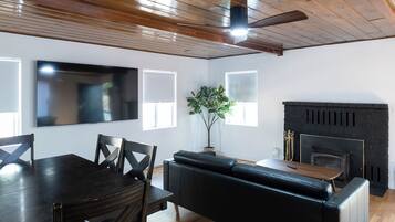 A modern living room with a dining area, a fireplace, and a ceiling fan.