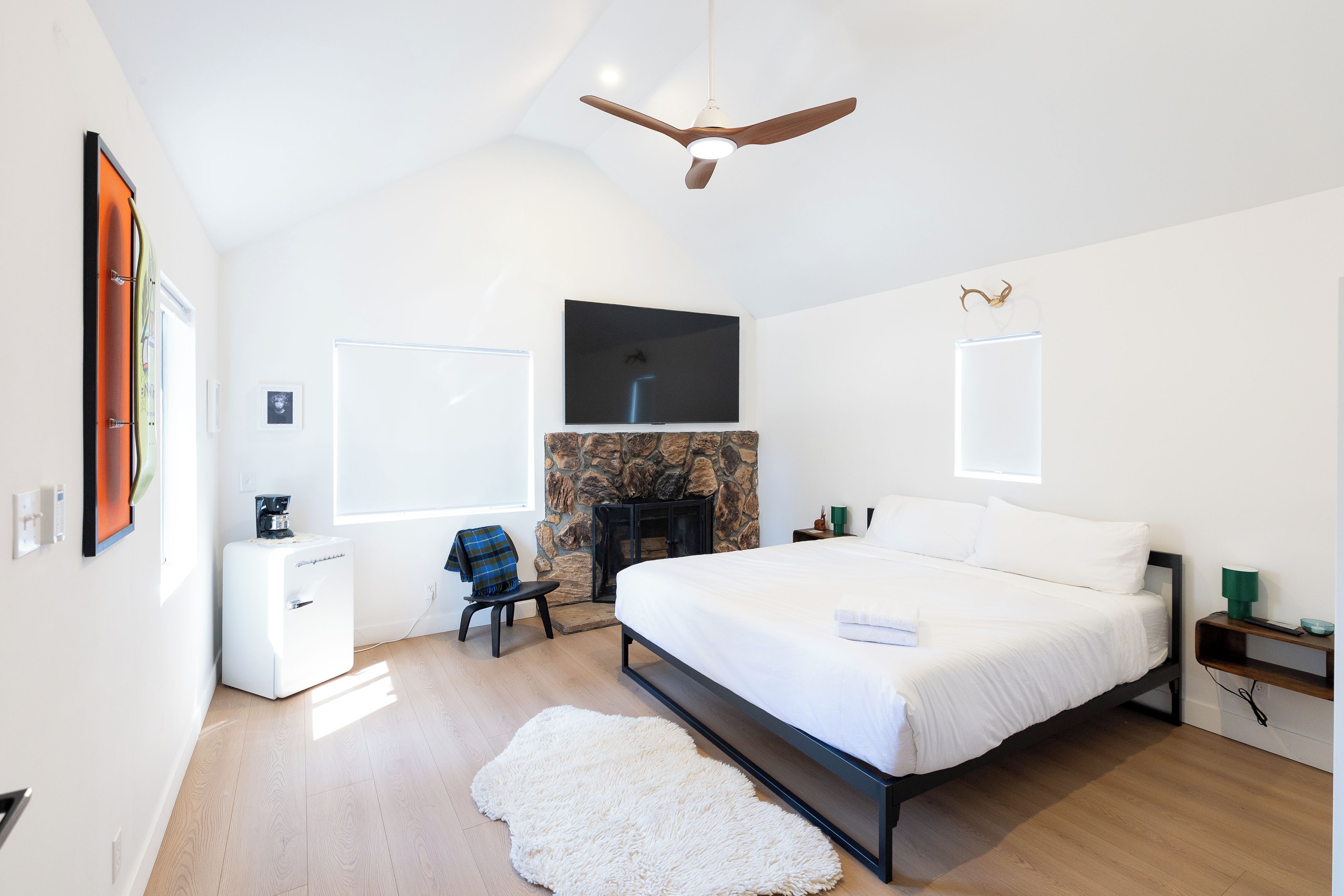 Un dormitorio moderno con una cama grande, una chimenea, un ventilador de techo y un televisor montado.