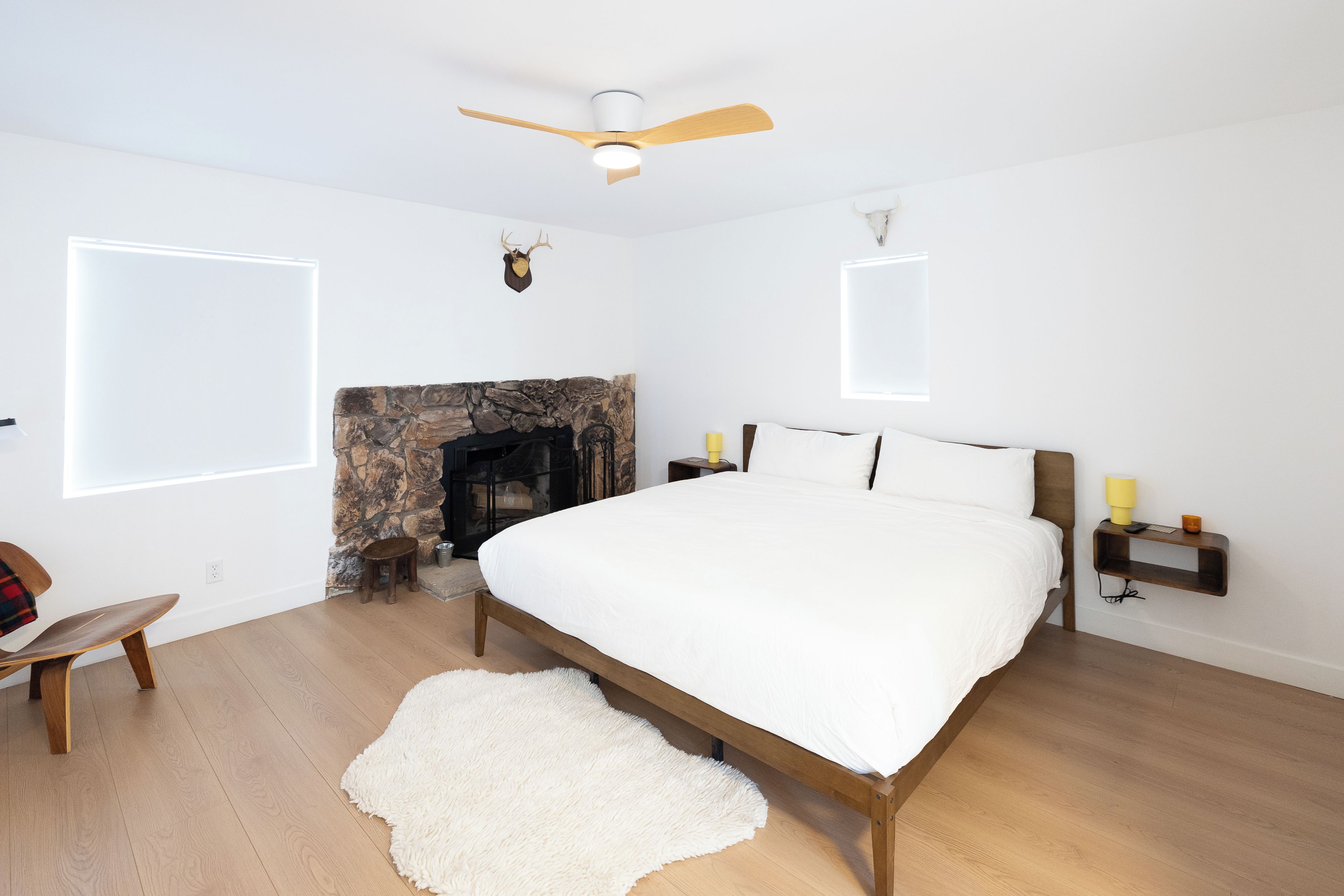 A bedroom with a bed, a fireplace, a ceiling fan, and a stone wall.