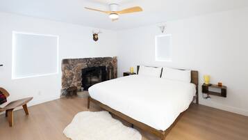 A bedroom with a bed, a fireplace, a ceiling fan, and a stone wall.