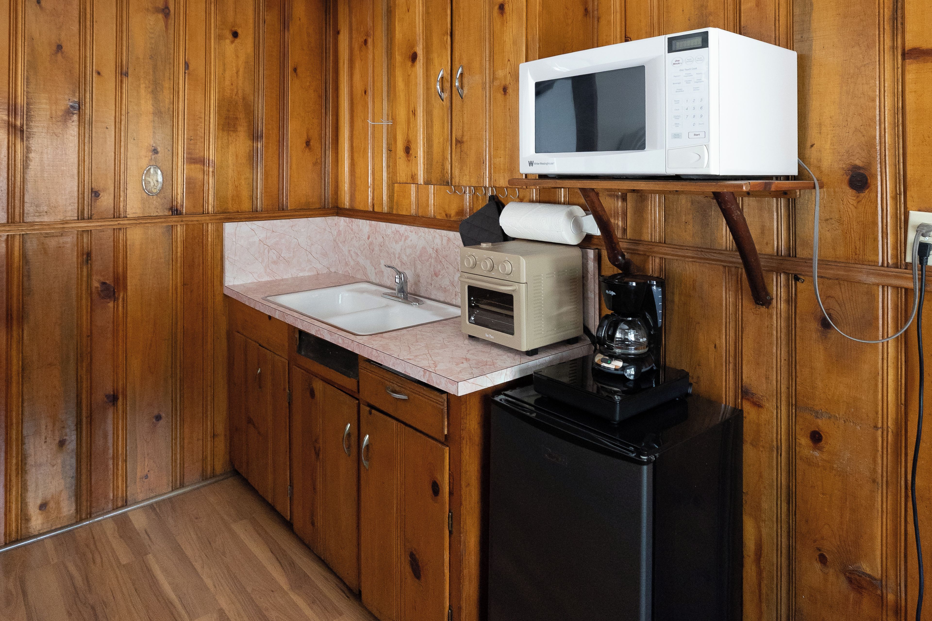 Een kleine keuken met houten kastjes, een gootsteen, een magnetron en een koffiezetapparaat.