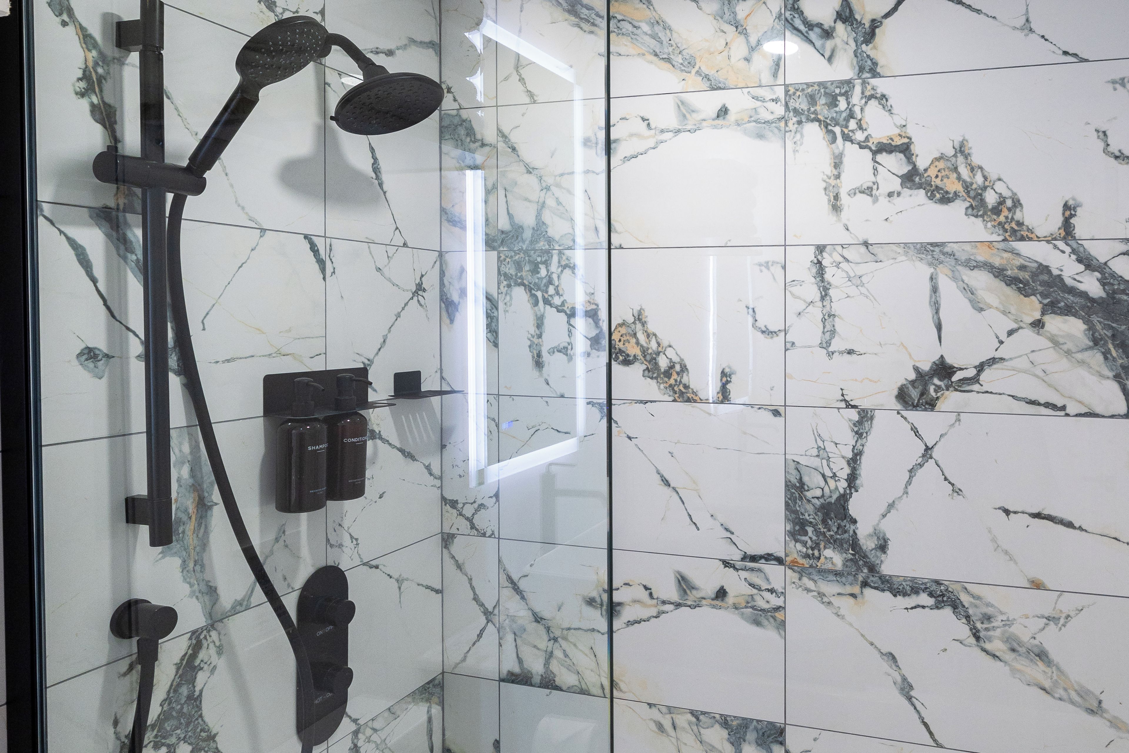 A bathroom with a shower, a mirror, and a glass partition.