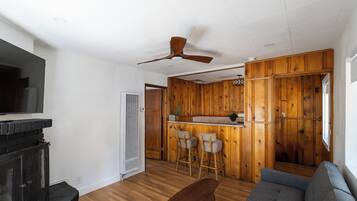 A living room with a fireplace, a ceiling fan, a sofa, and a kitchen area with wooden paneling.