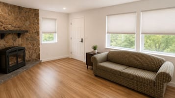 A living room with a stone fireplace, a sofa, and large windows with blinds.