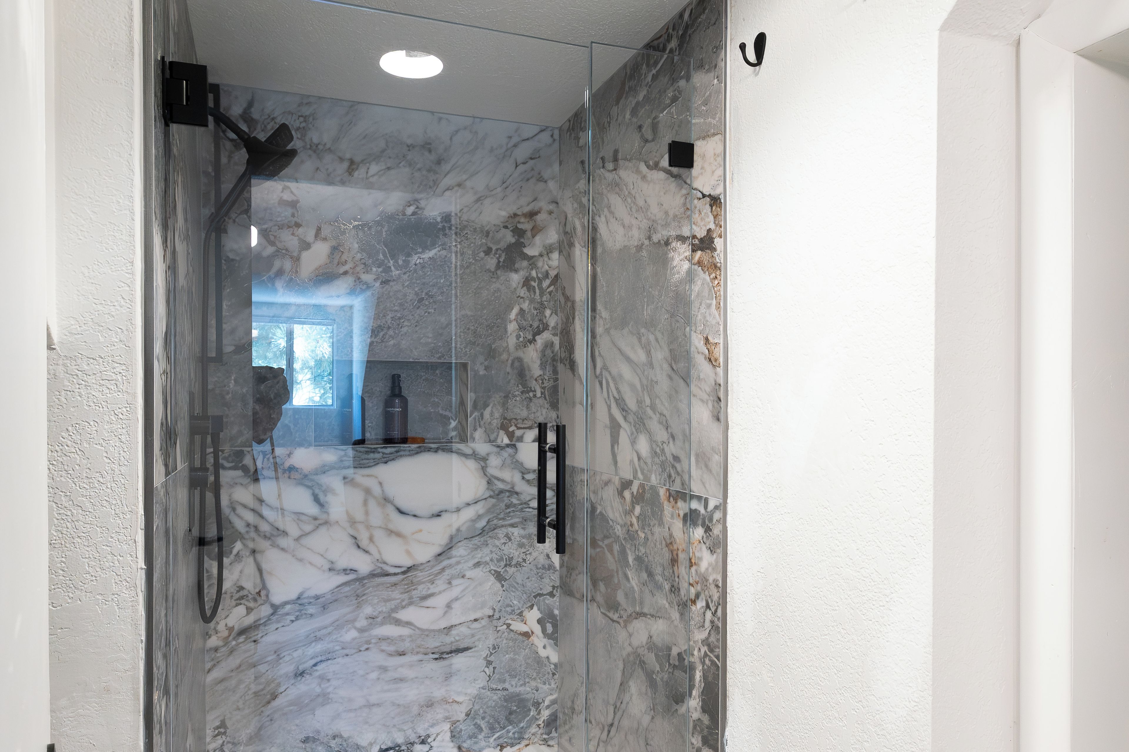 Un couloir aux murs de marbre et une porte en verre donnant sur une salle de bain.