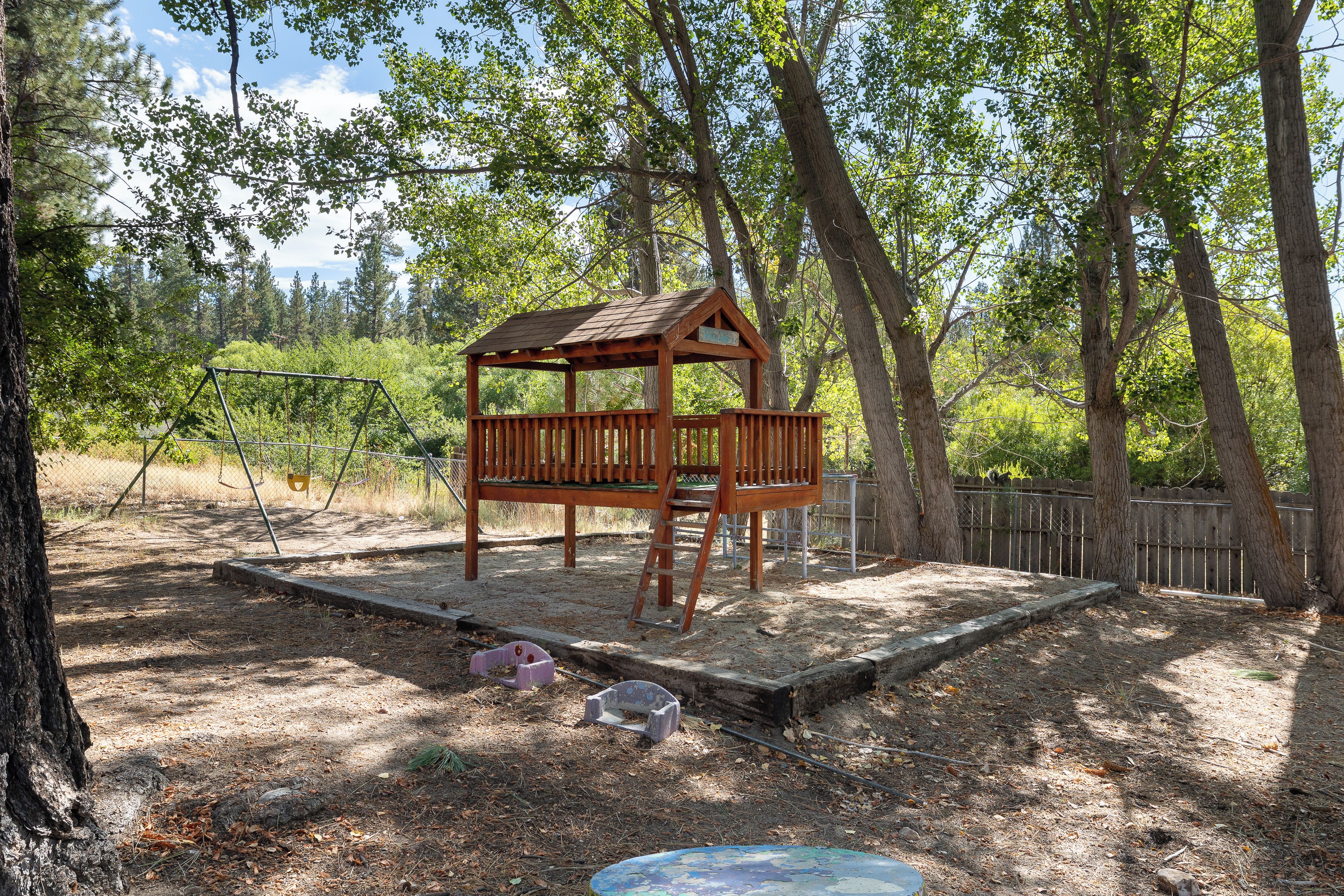 Une cabane en bois avec une échelle, entourée d’arbres et délimitée par une clôture.